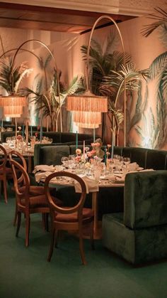 a dining room with green velvet chairs and palm trees on the wall behind tables set for dinner