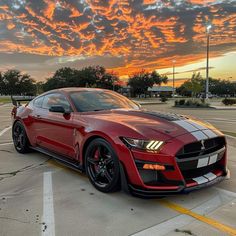 a red sports car parked in a parking lot with the sun setting on it's horizon