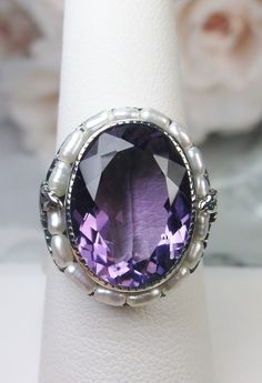 Natural Purple Amethyst & Pearl Ring Leaf Pearl Design#156 This is a stunning 9.5 carat natural purple amethyst gemstone ring. The natural amethyst gem has amazing color and clarity. This gemstone is 12mm x 16mm in dimensions (10/16" x 9/16"). The garden themed filigree circles the edge of the ring and extends down the band accenting the beautiful large gemstone. Seed pearls frame the large gemstone, creating a vibrant contrast. Holding the seed pearls in place are 2 silver leaves and fine w Exquisite Amethyst Ring For Wedding, Exquisite Amethyst Ring, Exquisite Amethyst Ring For Anniversary, Elegant Large Stone Amethyst Ring, Exquisite Purple Amethyst Ring For Anniversary, Exquisite Amethyst Ring With Gemstone Accents, Exquisite Silver Amethyst Ring, Exquisite Amethyst Gemstone Rings, Exquisite Purple Amethyst Ring With Gemstone Accents