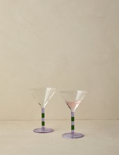 two wine glasses sitting on top of each other in front of a white wall and floor