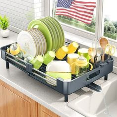 a dish rack filled with dishes in front of a window and an american flag outside