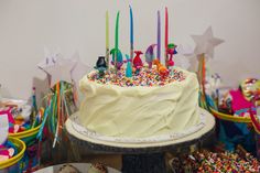 a birthday cake with candles and sprinkles on it sitting in front of other desserts