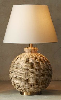 a wicker lamp with a white shade on the top is sitting on a table