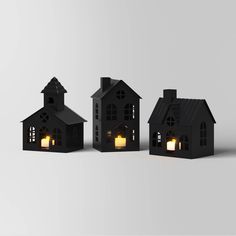 three small black houses with windows and lights on the front, one has a candle in it