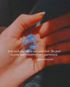 a woman's hand holding a small blue flower with the words live each day like it was your last the past is gone and tomorrow isn't quainted