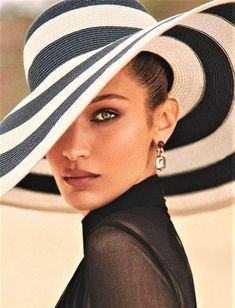 a woman wearing a black and white hat with stripes on the side, looking at the camera