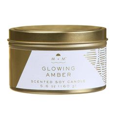 a candle in a gold tin with white labels on it that says, glowing amber scented soy candle