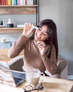 a woman sitting at a table with a laptop and looking up into the sky while holding something in her hand