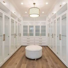 a large walk in closet with lots of white cabinets and mirrors on the walls, along with a round ottoman