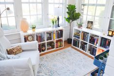 a living room filled with lots of books and furniture next to a white couch in front of a window