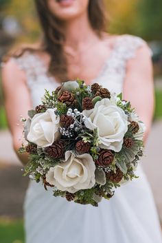 a bride holding a bouquet of flowers and pine cones