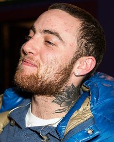 a man with tattoos on his face and neck looking off into the distance while wearing a blue jacket