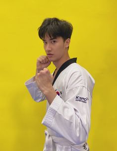 a young man standing in front of a yellow wall wearing a karate uniform and holding his fist up