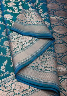 A Banarasi saree is a robust canvas where a weaver's unmatched craftsmanship, imagination, and creativity come to life! His dexterous hands beautifully blend the years of skills and experience to craft 6 yards of wearable art for the global woman of today's times. This saree is resplendent with all the elements of a rich Banarasi saree. The highlight of the drape is the intricately woven Floral jaal pattern on its rich body. The opulence of the drape is further enhanced by the traditional Banara Peacock Green Combination, Bridal Anklet, Trendy Outfits Indian, Banarsi Saree, Katan Silk Saree, Peacock Pattern, Katan Silk, Banarasi Saree, Stylish Sarees