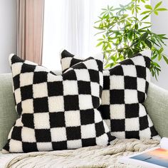 two black and white pillows sitting on top of a couch next to a plant in front of a window