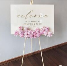 a welcome sign with pink flowers on it in front of a gray wall and wooden floor