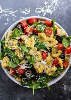 a white bowl filled with pasta salad topped with tomatoes, cheese and spinach leaves