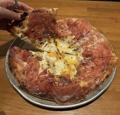 a person taking a slice of pizza from a metal pan on a wooden table top