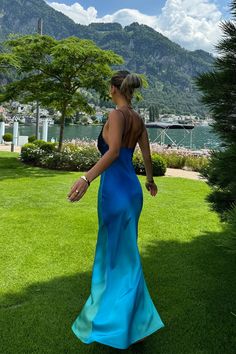 a woman in a blue dress is walking on the grass