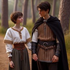 two people dressed in medieval clothing standing next to each other on a dirt road surrounded by trees