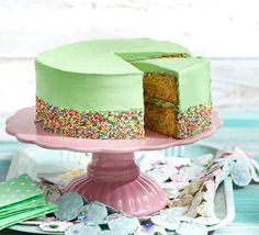 a green cake with sprinkles is on a pink plate and has one slice taken out