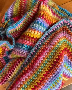 a multicolored crocheted blanket sitting on top of a wooden table next to a pair of scissors