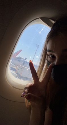 a woman with her fingers up in front of an airplane window