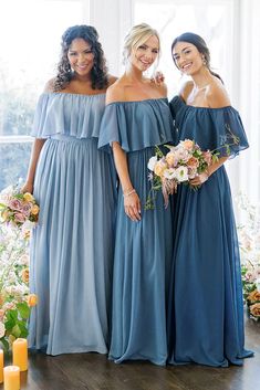 three bridesmaids in blue dresses standing next to each other near candles and flowers