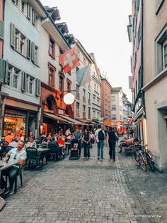 people are sitting at tables in the middle of an old city street with shops and restaurants