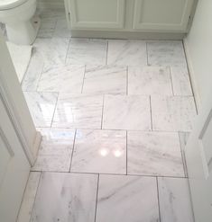 a bathroom with white marble flooring and tile on the walls, along with a toilet