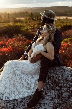 a man and woman sitting on top of a rock in the middle of a field