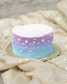 a multi - colored cake sitting on top of a white cloth covered in sequins