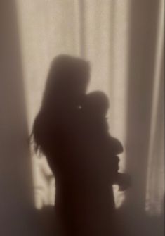 the shadow of two people standing next to each other in front of a white curtain