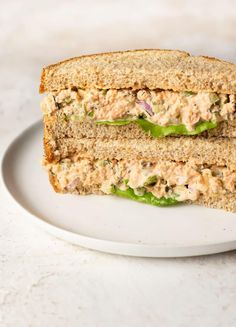 two halves of a sandwich on a white plate with green peppers and tuna in the middle