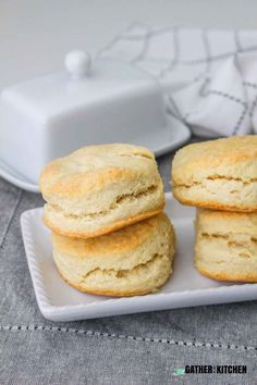 three biscuits sitting on top of a white plate next to a butter container and napkin