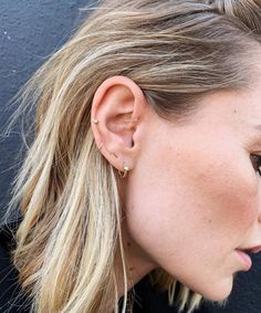 a woman with blonde hair wearing a pair of ear piercings in front of a black wall