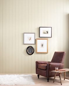 a brown chair sitting next to a wooden table in front of a wall with pictures on it