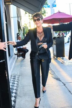 a woman in black suit and sunglasses walking down the street with her hand out to someone