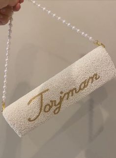 a person holding a white purse with the word jogan on it hanging from a chain