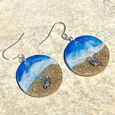 two sea turtles on the beach in blue and white earrings