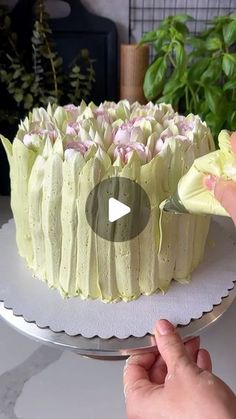 someone is decorating a cake with white frosting and pink flowers on the top