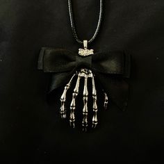 "This is a silver metal pendant featuring a creepy silver metal skeleton hand with a black ribbon bow at the top. It is hung from a black faux leather woven waxed cord that is 19 1/2\" long, with silver chain and a silver lobster claw clasp. Make sure to check out my shop for more hair pins, jewelry, accessories, and all sorts of fun stuff! Skeleton Hand, Black Bow, Bow Necklace, Silver Skeleton Hand, Hand Necklace, Skeleton Necklace, Skull Necklace, Black Ribbon" Black Skull Jewelry Grunge Style, Black Skull Shaped Grunge Jewelry, Black Skull Grunge Jewelry, Black Grunge Necklace For Gift, Punk Style Hand Cast Halloween Jewelry, Gothic Hand-cast Halloween Necklaces, Silver Skull Emo Jewelry, Black Skull Necklace For Halloween, Grunge Skull Jewelry For Gift