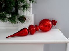 two red glass candy canes sitting on top of a white shelf next to a pine tree