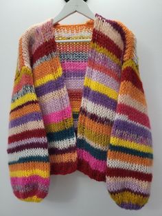 a multicolored cardigan sweater hanging on a white hanger with a black hook