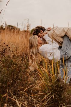 a couple kissing in the middle of a field with tall grass and weeds behind them