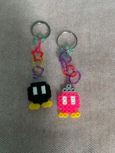 two lego key chains are sitting on a fabric surface, one is shaped like a car and the other has a pacifier in it's mouth