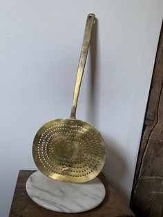 a large brass strainer sitting on top of a marble base next to a wall