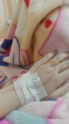 a hand with an iv attached to it laying on top of a pink and blue blanket