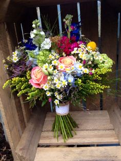 a bouquet of colorful flowers sitting on top of a wooden crate filled with grass and daisies