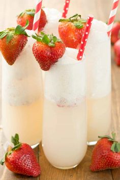 three glasses filled with ice and strawberries on top of a wooden table next to each other